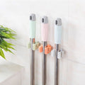 Three wall-mounted holders gripping cleaning-tool handles.
