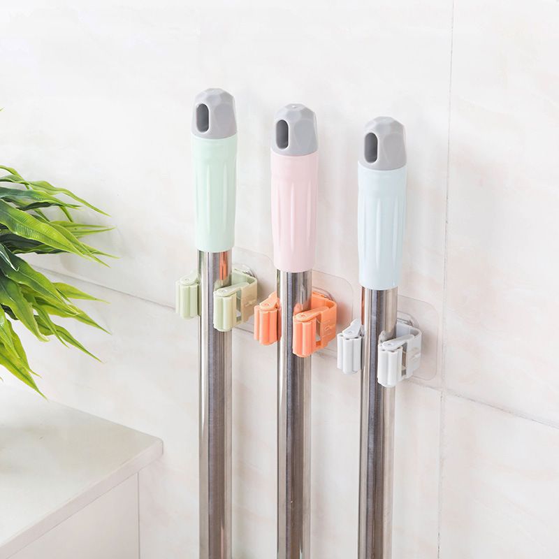 Three wall-mounted holders gripping cleaning-tool handles.