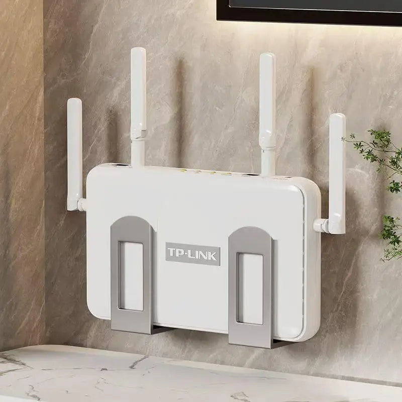 Gray wall-mounted router storage bracket holding a TP-Link Wi-Fi router flush against a marble-effect wall, with plants in the background