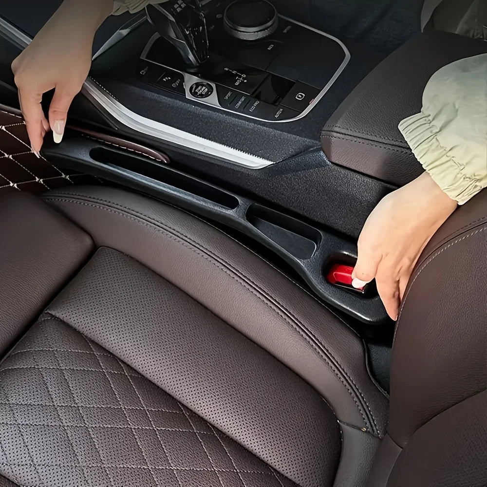 Person installing a black car seat gap filler organizer between the driver seat and center console, with seatbelt buckle visible in a dark brown leather interior