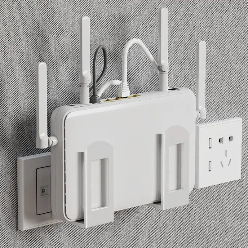 White wall-mounted router storage bracket holding a large Wi-Fi router with antennas and cables, mounted on a gray fabric wall next to a power outlet