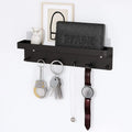 Black wall-mounted key holder with mail organizer shelf holding keys, a watch, necklace, and handcuff keychain on 6 hooks, with a wallet and owl figurine on the upper shelf, mounted on a white wall