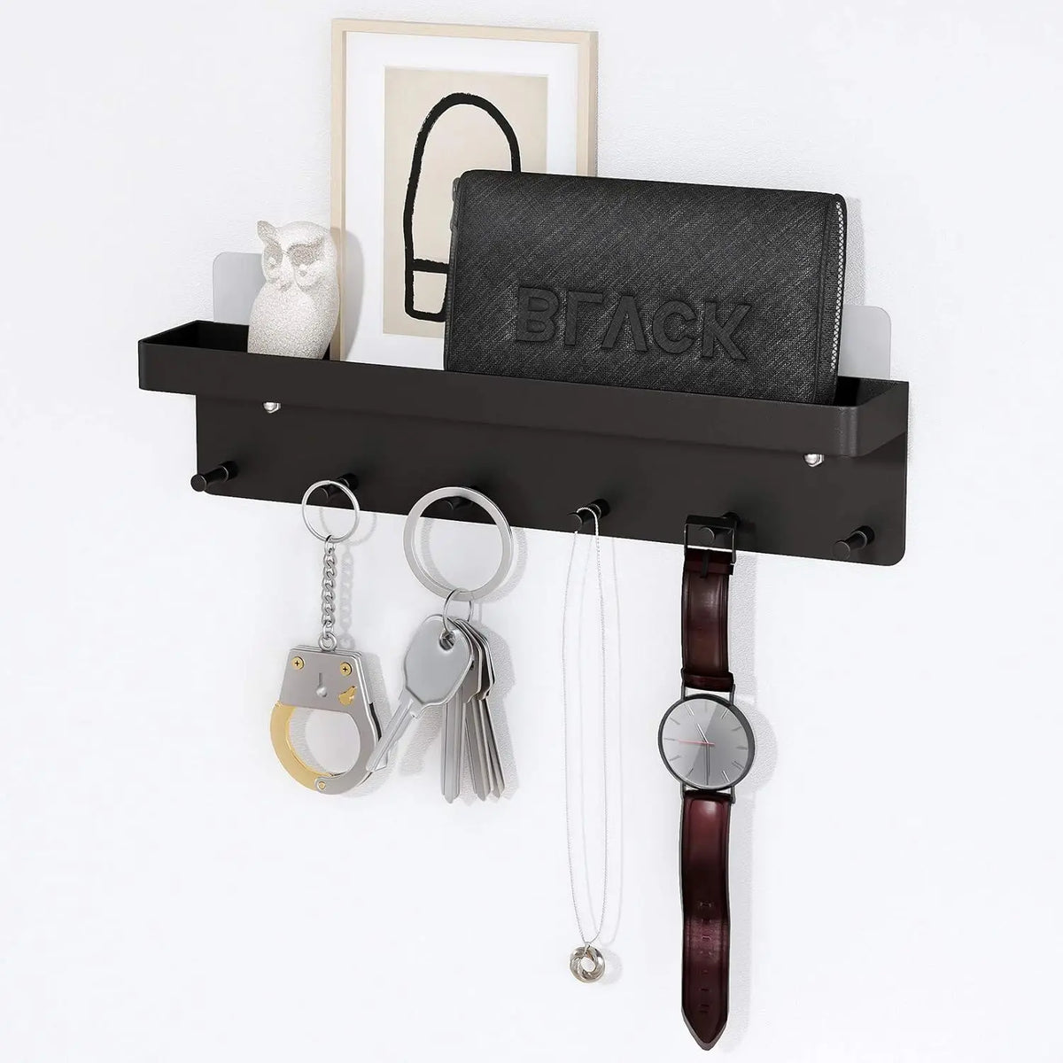 Black wall-mounted key holder with mail organizer shelf holding keys, a watch, necklace, and handcuff keychain on 6 hooks, with a wallet and owl figurine on the upper shelf, mounted on a white wall