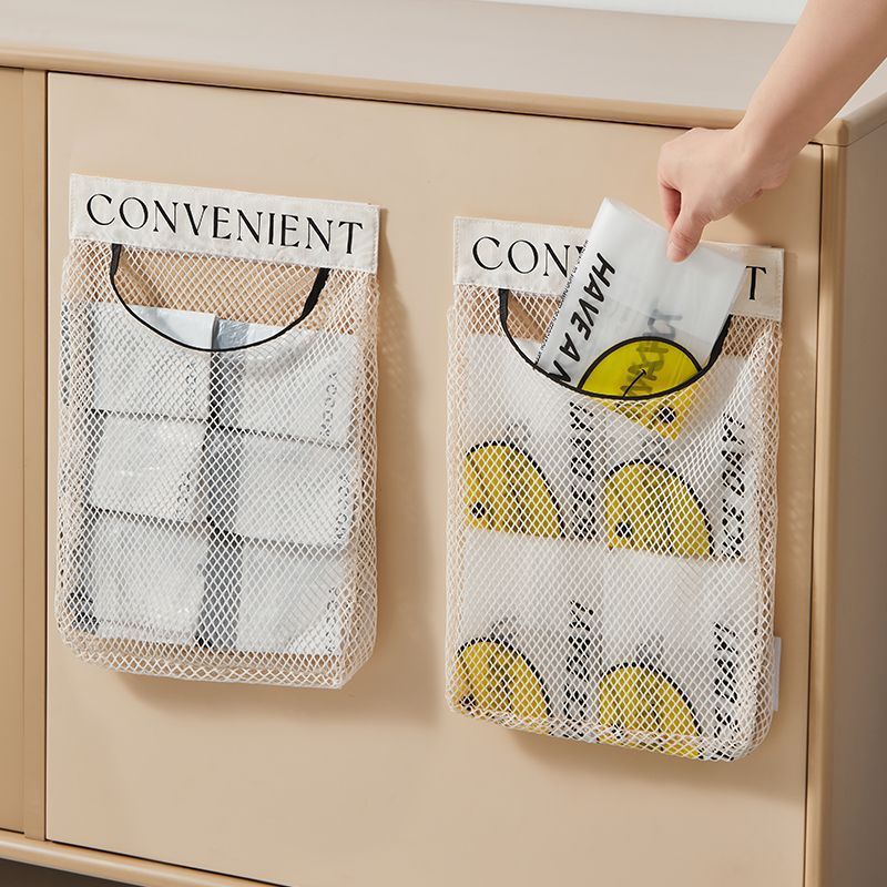 Two beige mesh storage bag organizers mounted on a beige cabinet door, one holding folded plastic bags and one with a hand pulling out a reusable grocery bag with yellow smiley face print